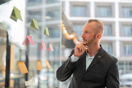 Determined Young Businessman Analyzing Sticky Notes in Modern Office Setting for Strategic Planning...