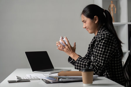 Stressed Young Accountant at Work with Laptop and Documents in Modern Office Environmentの写真素材