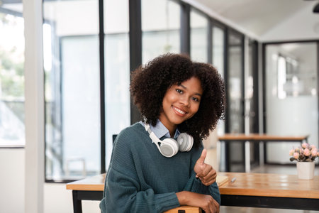 Young Woman Studying Online with Headphones, Smiling and Giving Thumbs Up in Modern Home Officeの写真素材