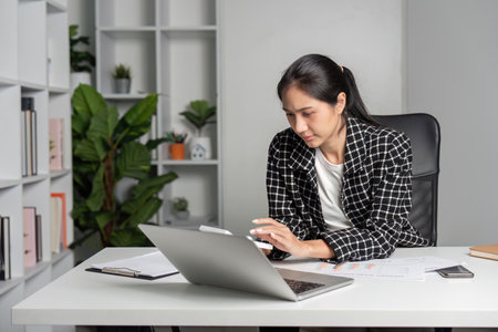Stressed Young Accountant Analyzing Financial Reports at Modern Office Desk with Laptop and Documentsの写真素材