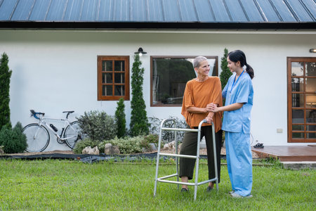 Elderly Woman with Caregiver Walking in Garden Outside Home, Enjoying Fresh Air and Nature, Senior Care and Support Conceptの写真素材