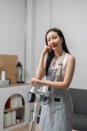 Young Woman Joyfully Cleaning Modern Home with Vacuum Cleaner in Bright and Stylish Living Room Settingの写真素材