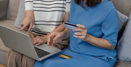 Mother and Child Shopping Online Together Using Laptop and Credit Card in Cozy Home Environmentの写真素材