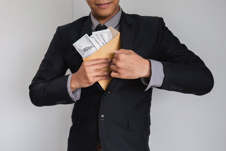 Businessman Hiding Money in Envelope Symbolizing Corruption and Financial Misconduct in Corporate Environmentの写真素材