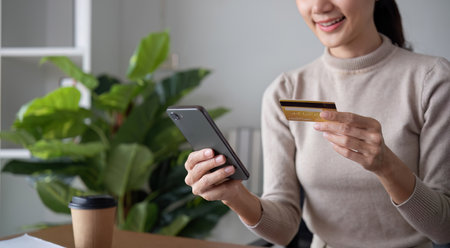 A person uses a phone and credit card for online shopping while sitting at home.