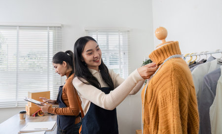 Women fashion designers adjusting a cozy sweater on a mannequin, showcasing teamwork and creativity in a boutiqueの写真素材