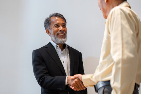 Smiling male businessman in a suit shaking hands during a successful deal negotiationの写真素材