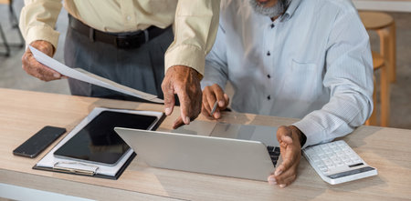 Elderly businessman collaborating with colleague on financial calculations in modern office