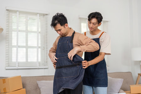 LGBT couple sharing warm moments while dressing in aprons, supporting each other at homeの写真素材