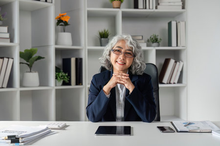 Confident elderly businesswoman smiling at her desk in a stylish modern office settingの写真素材