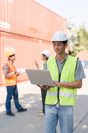 Construction worker using a laptop to manage projects while colleagues discuss plans on-site