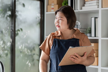 Businesswoman analyzing plans with a clipboard in a modern workspace during a strategy meetingの写真素材