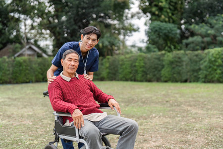 Nursing aide proudly standing behind elderly man in wheelchair, showcasing support and companionship in a gardenの写真素材