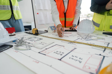 Construction team working on detailed plans with measuring tools and hard hats in a modern office spaceの写真素材