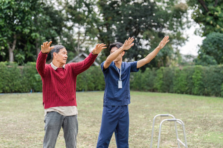 Health caregiver guiding elderly man through physical exercise in the park for rehabilitationの写真素材