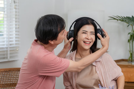 Mature couple sharing music and laughter with headphones at home.の写真素材
