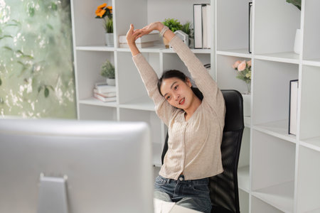 Woman stretching and relieving tension at her office desk during work.