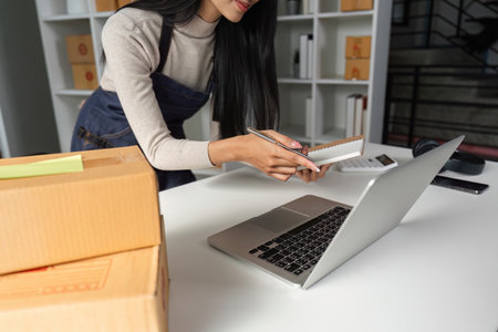 Entrepreneur organizing packages and taking notes in a contemporary office space.の写真素材