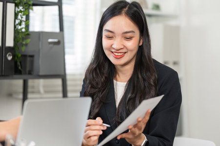 Professional businesswoman reviewing documents and collaborating in a modern office settingの写真素材
