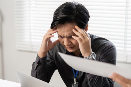 Stressed male colleague struggling with project details while female professional offers guidance in a modern office.の写真素材