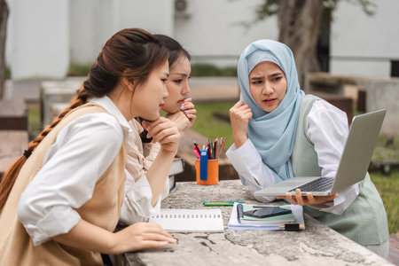 Female students focusing on a laptop screen during a study session outdoors.