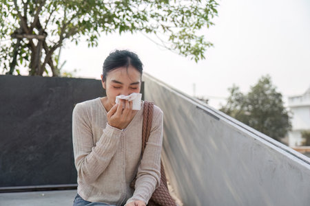 Young woman experiencing discomfort due to pollution, using tissue outdoorsの写真素材