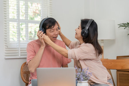 Senior couple playfully sharing headphones while enjoying music at home.の写真素材