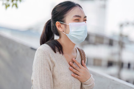 Cheerful woman in a mask smiling while using her smartphone.の写真素材