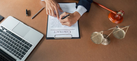 Lawyer signing contract document while reviewing legal paperwork at desk with laptop and gavel.