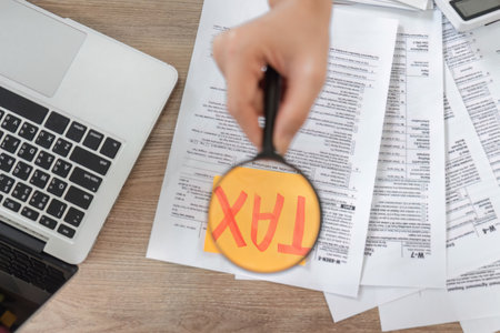Close-up of hands using a magnifying glass on tax documents, emphasizing important financial information.の写真素材