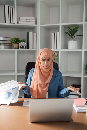 Diverse female accountant expressing confusion while reviewing financial reports on a laptop in an office.の写真素材