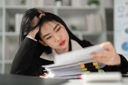 Frustrated businesswoman analyzing tax paperwork, highlighting the challenges of financial management.の写真素材