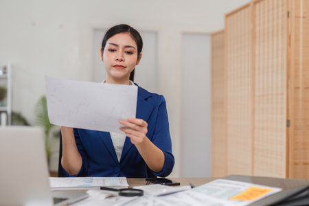 Focused businesswoman analyzing financial statements with coffee in hand, preparing for tax season.の写真素材
