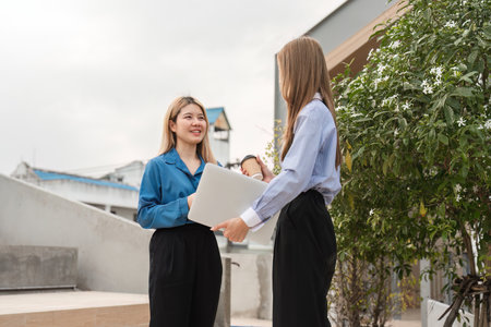 Diverse businesswomen engaging in conversation while holding a laptop outdoors.の写真素材