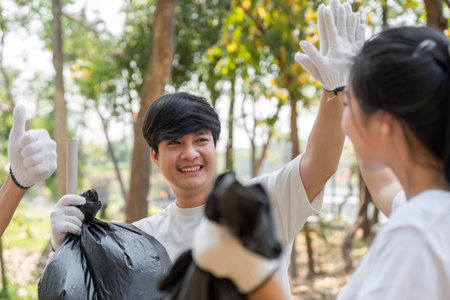 Smiling young man celebrating a successful cleanup with friends, emphasizing teamwork and environmental care.の写真素材