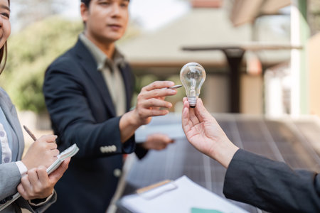 Sustainable business strategies. Professionals discussing energy-saving solutions with a light bulb.の写真素材