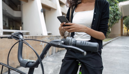 Sustainable Living and Connectivity. A woman checking her phone while parked on her bicycle in an urban setting.の写真素材