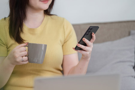 Digital Connectivity and Relaxation. A woman using her phone with a coffee cup, enjoying moments in...