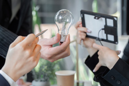 Innovation and Eco-Friendly Solutions. A professional team discusses energy-saving concepts, showcasing a light bulb.の写真素材