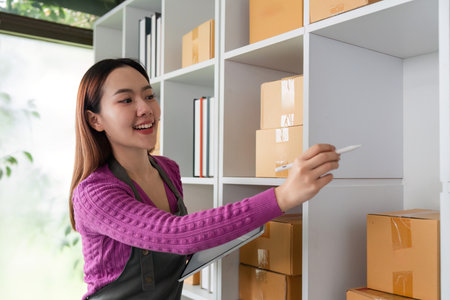 Online Selling and Inventory Management. A cheerful woman labeling packages in her organized workspace, demonstrating efficient online selling practices.の写真素材