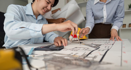 Teamwork and Blueprint Analysis. A focused architect using a compass to finalize the layout of a building design, collaborating with colleagues.の写真素材