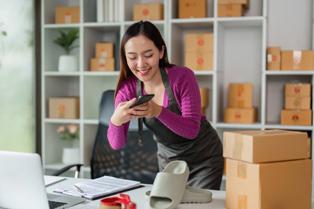Sales Promotion and Product Interaction. A smiling woman using her phone in a workspace, blending technology and customer engagement in her online selling business.の写真素材