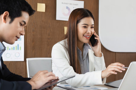 Mobile Business Communication and Productivity. A professional on the phone while working on a laptop during a meeting.の写真素材