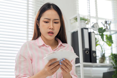 Financial Stress and Home Office Challenges. A woman with a worried expression examining her bills in her workspace.の写真素材