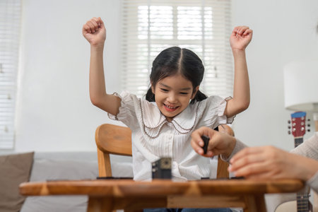 Winning Smiles and Family Games. A girl celebrates her victory while playing a game with her mother.の写真素材