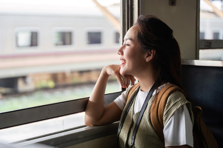 Reflections and Travel Dreams. A woman gazes out of a train window, smiling at the world passing by.の写真素材
