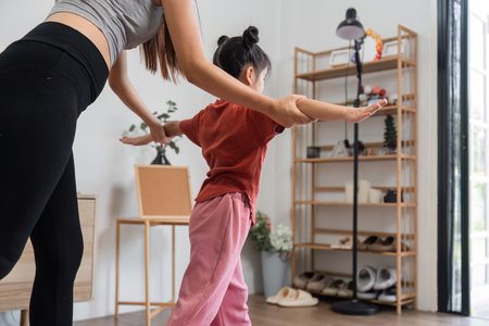 Balance and Fitness Fun. A mother guiding her daughter in maintaining balance during a home workout.の写真素材