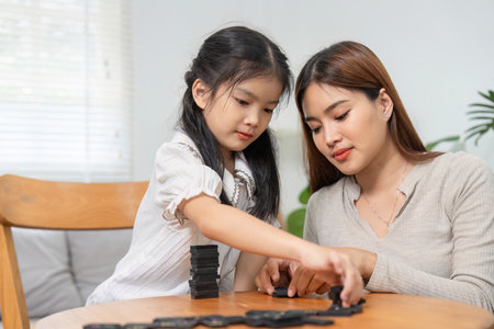 Connection and Playtime. A mother supporting her daughter as they play with dominoes together at the...