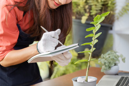 Journaling and Plant Observation. A woman records observations about her potted plant for sustainable gardening.の写真素材