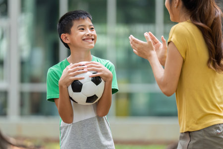 Encouragement and Growth in Sports. A young boy smiles at his mother, excited to play soccer, as she shows support.の写真素材